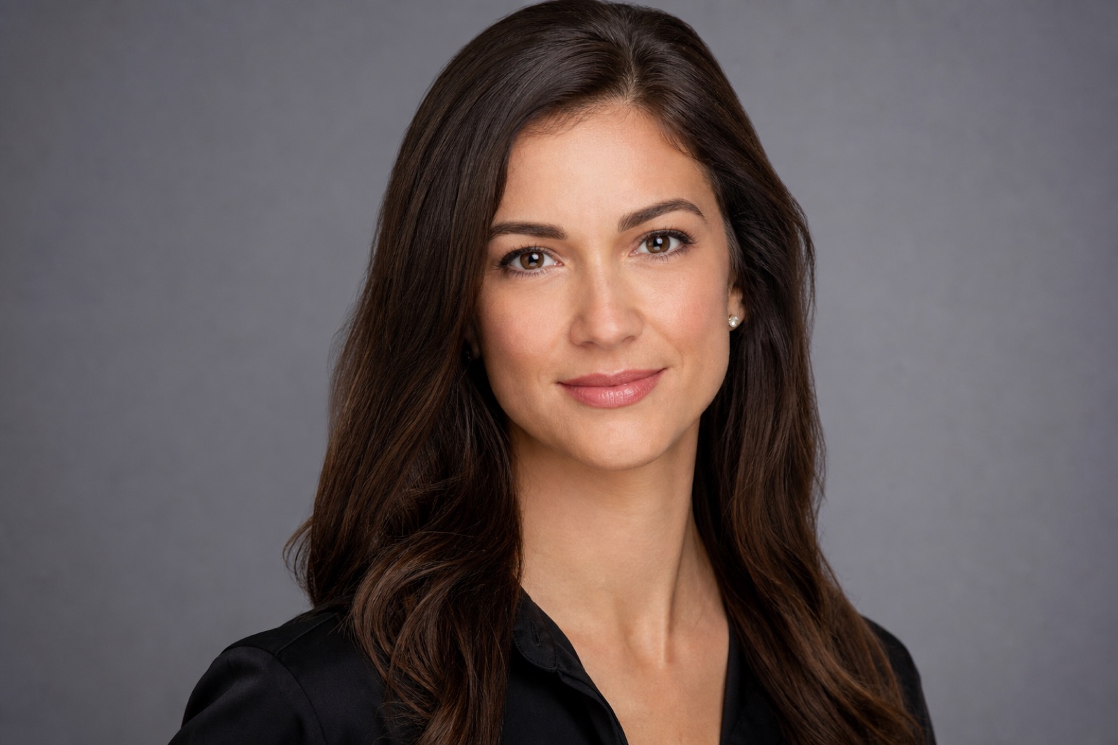 Studio portrait of a woman against a plain charcoal backdrop, lit with a single soft key light